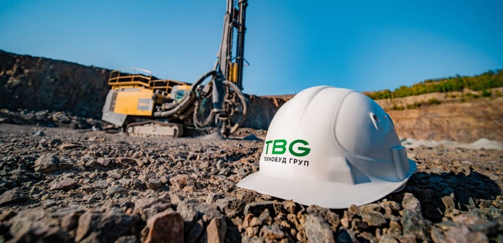 Каска з логотипом Технобуд Груп а позаду буровий станок на Клесівському кар'єрі Технобуд